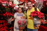 Productores michoacanos sostienen plantas de nochebuena de color rojo en un vivero, durante la temporada navideña, reflejando la importancia económica y cultural de este cultivo en el estado.