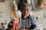 Alejandrino García Méndez, maestro de los voladores de Papantla, sostiene una figura tradicional del danzante dentro de un espacio comunitario en Veracruz.