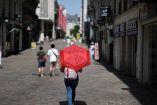Una persona caminando por una calle peatonal de tiendas en Nantes, sosteniendo un paraguas rojo abierto como parasol para protegerse del sol abrasador.