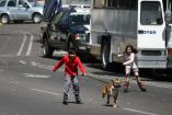 Un par de niños patinan en  la calle felices con su perro