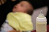 Un bebe en segundo plano, en primero su mamila con leche
