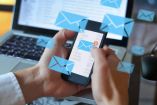 manos sostienen un teléfono con icono de correo electrónico y computadora al fondo