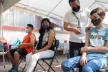 Un joven está recibiendo la vacuna, mientras dos más están esperando