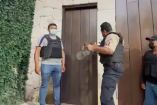 Tres policías, dos con chaleco tratan de abrir una casa por una orden de cateo