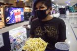 Una joven se prepara con sus palomitas y refresco para entrar a una sala de cine.