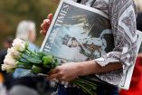 Una mujer carga un ramo de flores blancas junto a un periódico con la noticia del deceso de Isabel II.