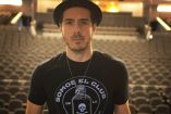 José Madero con sombrero y playera negra y butacas de auditorio atrás