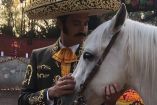 Jaime Camil con sobrero y traje de charro acariciando caballo blanco