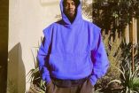 Kanye West con manos en bolsas, sudadera morada y gorro en cabeza