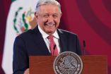 AMLO de traje oscuro, corbata roja y sonriendo