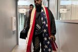 Kanye West caminando con vestuario negro y bandera de Estados Unidos en cuello