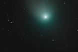Cometa verde, estrellas a un lado y cielo oscuro atrás
