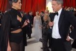 Hugh Grant con micrófono enfrente de periodista Ashley Graham