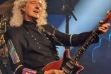 Brian May con camisa negra y guitarra en concierto