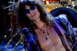 Steven Tyler con lentes y camisa abierta; batería atrás