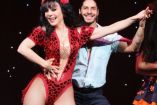 Maribel Guardia con vestido rojo escotado bailando con hombre en obra de teatro