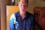 Joshn Homme con camisa azul adentro de casa; mueble atrás
