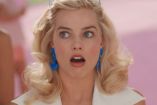 Margot Robbie con cara de sorprendida, usando lentes y aretes azules