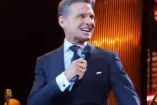 Luis Miguel cantando en concierto, usa traje negro y micrófono