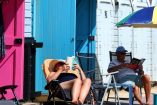 Grupo de personas relajándose junto a coloridas casetas de playa en Bournemouth, Reino Unido, en un soleado día de agosto de 2023.