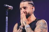 Maluma con trenzas y manos en cara; enfrente de micrófono