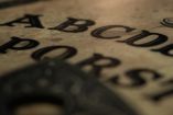 tablero de ouija con puntero encima y vela prendida