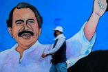 Persona pasando junto a un mural vibrante de Daniel Ortega, presidente de Nicaragua, con el brazo levantado en un gesto de poder