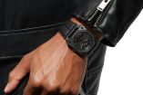 Hombre posa reloj, vestido todo de negro 