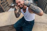 J Balvin con manos en la boca sentado al borde de un edificio