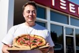 Elon Musk sosteniendo una pizza frente a local de Tesla.