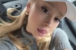 Ariana Grande sacando lengua, con gorra blanca y blusa gris
