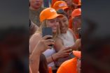 Dos mujeres sonrientes, una tomando una selfie, en un evento de campaña, rodeadas de seguidores con gorras naranjas del partido Movimiento Ciudadano, simbolizando la participación ciudadana y el apoyo a los emprendedores locales en Monterrey.