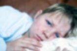 Niño pálido y enfermo en cama, con mirada fatigada, ilustrando el impacto del sarampión en los menores y la importancia de la vacunación.