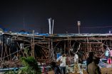 Equipos de rescate en una gasolinera en Bombay, India, retirando escombros de una valla publicitaria colapsada tras una fuerte tormenta. Varias personas observan la escena mientras los socorristas buscan sobrevivientes entre los restos.