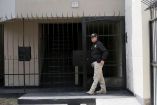 Un oficial de policía se encuentra de pie frente a la entrada de una residencia en Lima, Perú. La imagen muestra la fachada de un edificio con una puerta negra de rejas y el número "127" visible en la parte superior. Esta vigilancia está relacionada con una investigación en curso por presunto tráfico de influencias, implicando a miembros de la familia de la presidenta peruana Dina Boluarte.