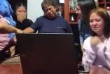 Mujer y joven llorando con familia frente a computadora