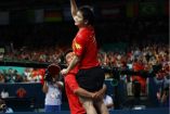 Zhendong con la mano en el aire mientras su entrenador lo carga celebrando la victoria