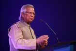 Muhammad Yunus hablando en un podio durante un evento, conocido por su impacto global en microfinanzas y su reciente nombramiento como líder de un gobierno interino en Bangladesh.