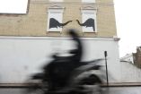 Escena urbana capturando a un motociclista en movimiento frente a un mural de Banksy que muestra dos elefantes en las ventanas de un edificio, simbolizando posiblemente la rapidez de la vida urbana contrastada con la serenidad del arte callejero.