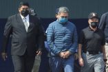 El expresidente de Honduras, Juan Orlando Hernández, es escoltado por agentes mientras es llevado con las manos esposadas, vistiendo una chaqueta azul y mascarilla, después de ser extraditado a Estados Unidos para enfrentar cargos de narcotráfic