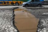 Bache en calle, lleno de agua y carro pasando