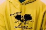 Sudadera amarilla con el logo de "Bailando en la Lluvia" de Daddy Yankee, mostrando una nube negra con brazos y piernas que parece estar bailando bajo la lluvia, reflejando el tema de resiliencia del sencillo.