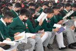 Alumnos de secundaria sentados en bancas con libros en las manos