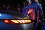 Imagen que muestra las luces traseras LED de un vehículo moderno en una exhibición automotriz. Al fondo, varias personas observan el auto, destacando el interés por la innovación y tecnología de los vehículos actuales.