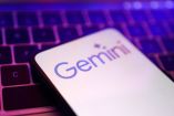 Primer plano de un smartphone con la pantalla mostrando el logo de Gemini, el asistente de inteligencia artificial de Google, sobre un teclado iluminado en tonos morados y rosas.