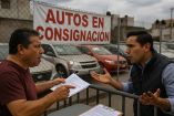 Dos hombres discuten en la entrada de un lote de autos usados en México; al fondo un letrero de "Autos en consignación", simbolizando los conflictos frecuentes por fraudes en este tipo de negocios.