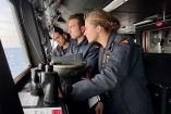 La Princesa Leonor, con uniforme de guardiamarina, observa el horizonte desde el puente de mando de la fragata Blas de Lezo durante una jornada de instrucción militar en Ceuta. La acompañan dos compañeros cadetes. Imagen captada en junio de 2025 como parte de su formación en la Armada Española.