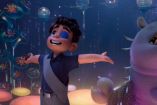 Elio, un niño de once años, sonríe con los brazos extendidos en un entorno galáctico iluminado por esferas flotantes y criaturas alienígenas. A su lado, una criatura amistosa muestra una gran boca sonriente. La escena refleja el espíritu de aventura y descubrimiento de la nueva película de Pixar.