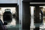 Estacionamiento subterráneo en la colonia Agrícola Pantitlán, Ciudad de México, completamente inundado tras lluvias intensas. Varios autos, con cofres abiertos y marcas de agua, permanecen sumergidos a media altura mientras un trabajador de la alcaldía realiza labores de desazolve.
