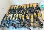 Imagen de más de 20 rifles de asalto tipo AR-15 alineados sobre una tarima de madera, asegurados por elementos del Ejército Mexicano durante un operativo en Sinaloa; las armas están etiquetadas como evidencia y forman parte de un decomiso federal en un inmueble cateado.